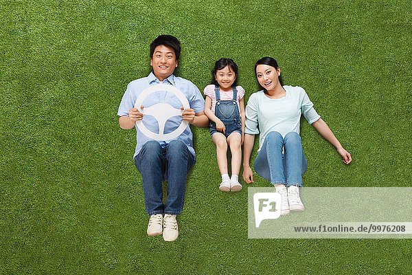 The joy of a family of three in lying on the grassland is holding the steering wheel model