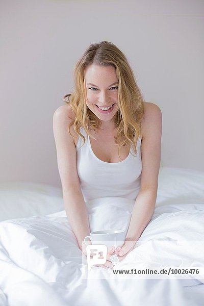 Frau Fröhlichkeit lächeln Bett Blick in die Kamera trinken blond hübsch Tee