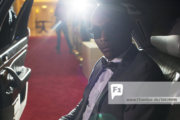 Portrait of serious celebrity in sunglasses inside limousine arriving at red carpet event