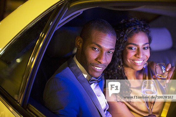 Well-dressed couple drinking champagne inside limousine