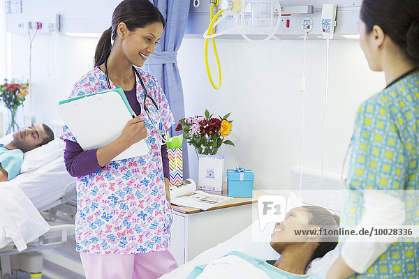 Smiling nurses talking with patient in hospital room