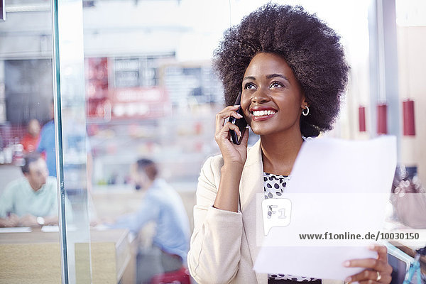 Lächelnde Geschäftsfrau mit Papierkram am Telefon