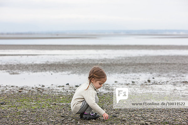 Mädchen sammelt Kieselsteine am Strand auf
