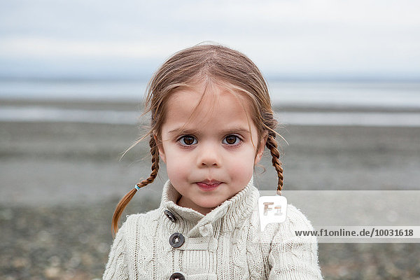 Porträt eines ernsthaften Mädchens mit geflochtenen Zöpfen am Strand