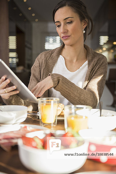 Mid adult woman using a digital table at breakfast table  Munich  Bavaria  Germany