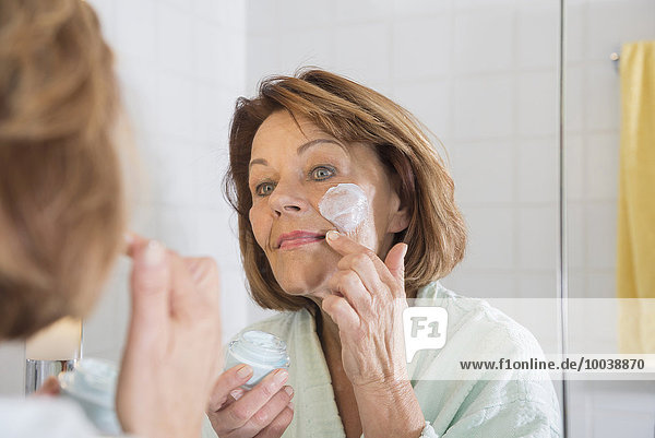 Reflection of a senior woman applying moisturizer on her face in mirror  Munich  Bavaria  Germany
