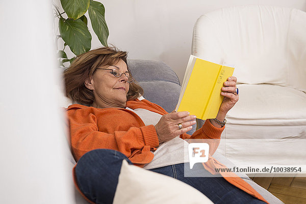 Senior woman reading a book while lying on sofa at home  Munich  Bavaria  Germany