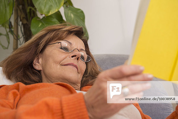 Senior woman reading a book while lying on sofa at home  Munich  Bavaria  Germany