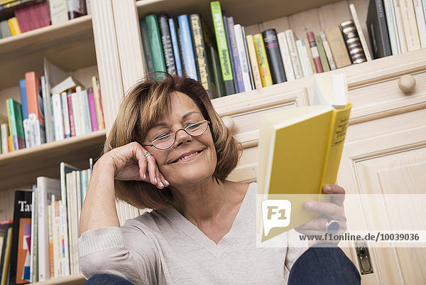 Senior woman sitting in front of bookshelf and reading  Munich  Bavaria  Germany