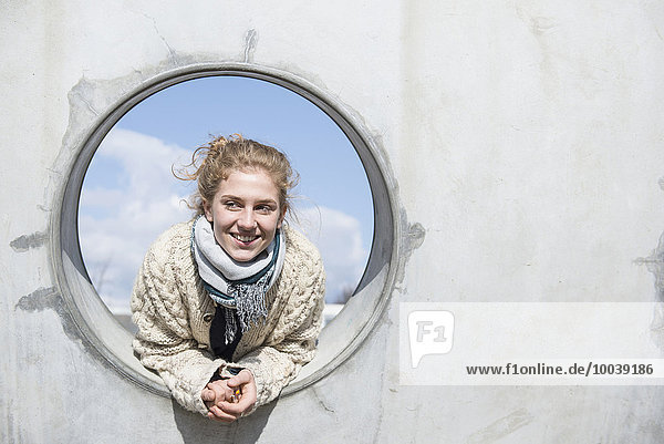 Young woman looking through a round hole in concrete wall  Munich  Bavaria  Germany