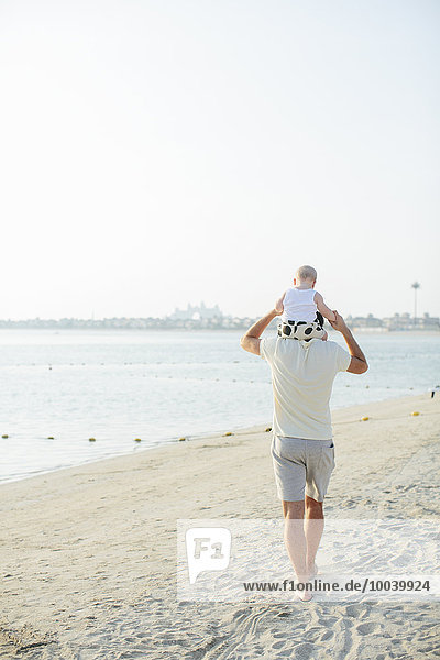 father carrying baby on shoulders at beach