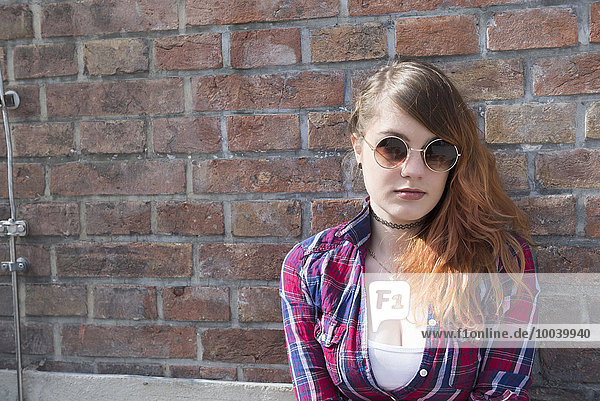 Young woman leaning in front of brick wall  Munich  Bavaria  Germany