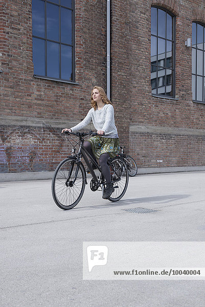 Young woman riding a bicycle in front of brick wall  Munich  Bavaria  Germany