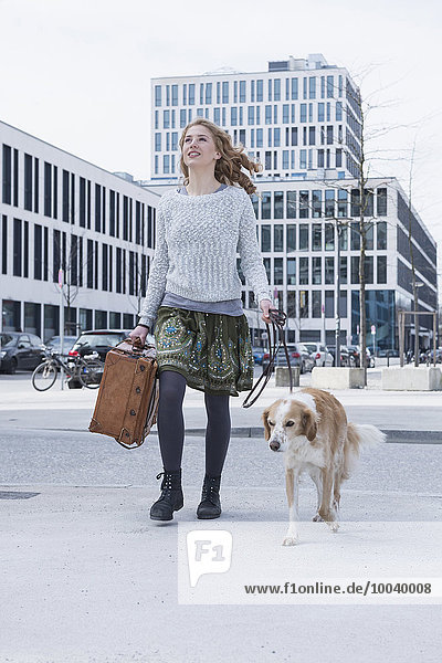 Young woman walking on road with dog and suitcase  Munich  Bavaria  Germany