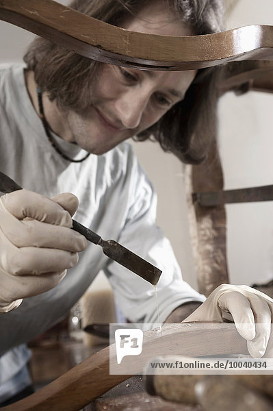 Carpenter applying glue on antique wooden chair at workshop  Bavaria  Germany