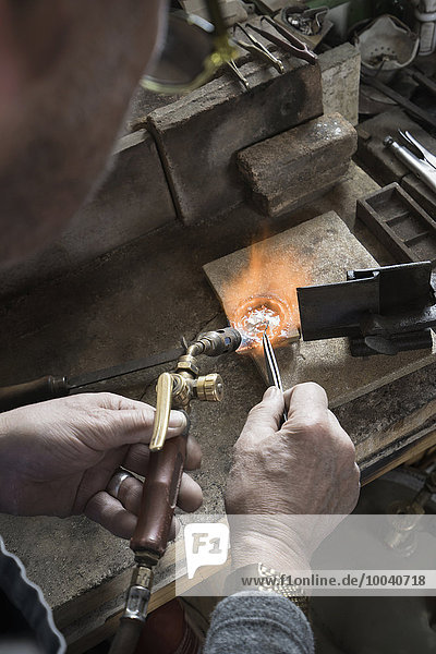 Senior male goldsmith melting and casting with blow torch at workshop  Bavaria  Germany