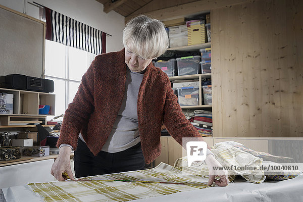 Senior female fashion designer measuring fabric in workshop  Bavaria  Germany