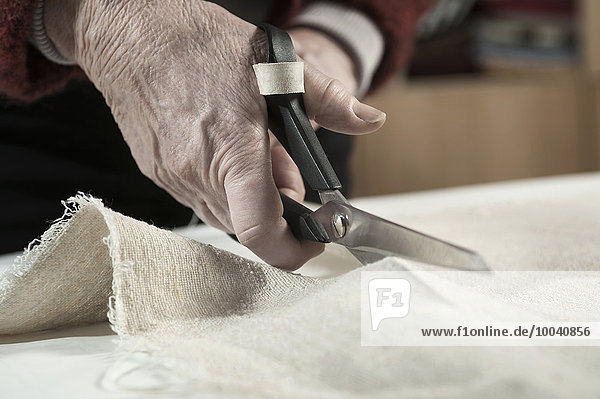 Senior female fashion designer cutting fabric with scissors in workshop  Bavaria  Germany