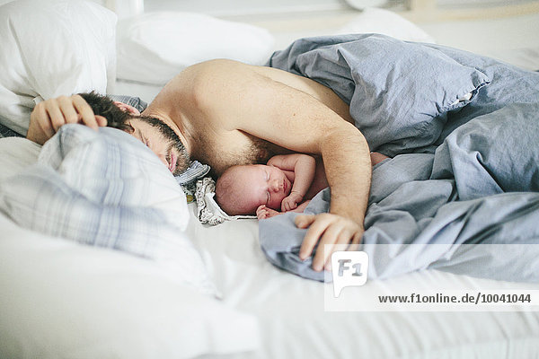 Man with newborn baby sleeping in bed