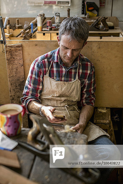 An antique furniture restorer in his workshop  using a smart phone.