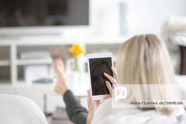 Rückansicht der blonden Frau mit Mini-Tablette zu Hause