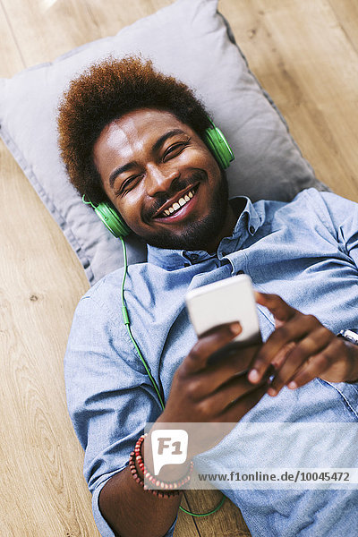 Young Afro American man lying on floor with headphones and smart phone