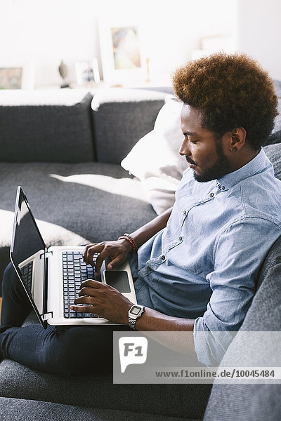 Young Afro American man sitting on couch  using laptop