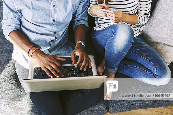 Young couple sitting on couch  using laptop and smart phone