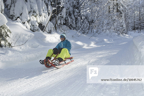 Germany  Bavaria  Inzell  man having fun on a sledge in snow-covered landscape