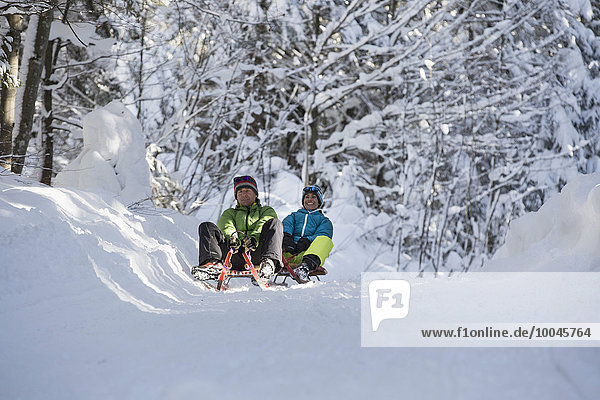 Germany  Bavaria  Inzell  couple having fun on sledges in snow-covered landscape