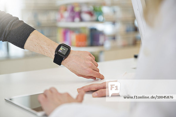 Customer showing female pharmacist his smartwatch