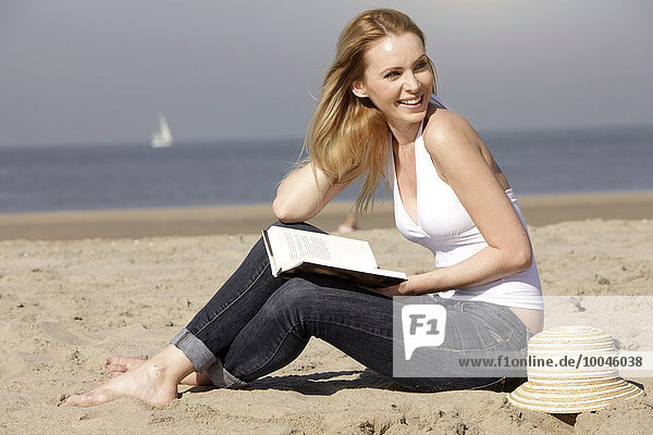 Niederlande  Scheveningen  junge Frau mit Buch am Sandstrand sitzend