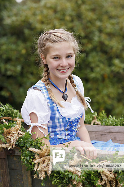 Germany  Luneburger Heide  portrait of smiling blond girl wearing dirndl sitting on harvest wagon