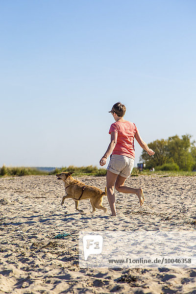 Deutschland  Kiel  Frau läuft mit ihrem Hund am Sandstrand