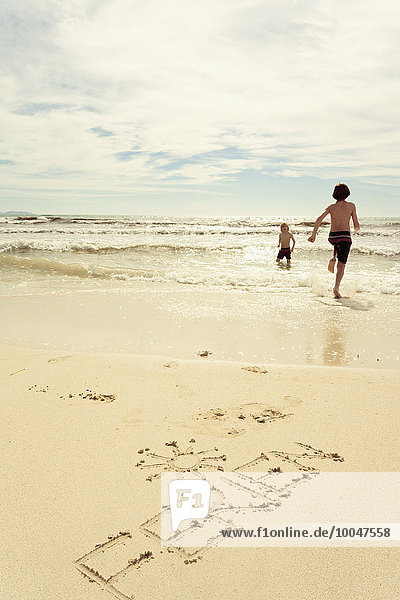 Spanien  Mallorca  Zwei kleine Jungen am Strand laufen ins Meer  Wort Ferien im Sand geschrieben