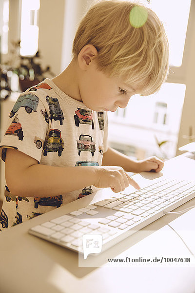 Blond little boy typing on the keyboard of a computer