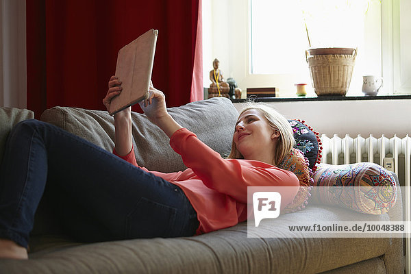 Lächelnde junge Frau entspannt mit digitalem Tablett auf der Couch zu Hause