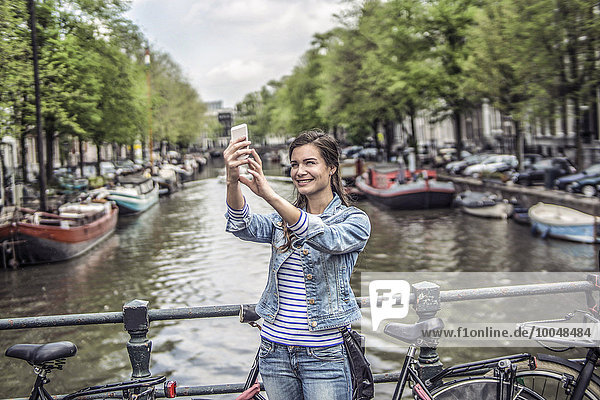 Niederlande,  Amsterdam,  Touristin mit Smartphone vor dem Stadtkanal