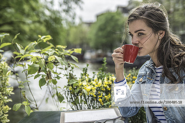 Niederlande  Amsterdam  Frau  die in einem Straßencafé eine Tasse Kaffee trinkt.