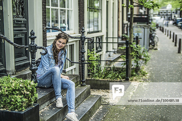 Niederlande Amsterdam lächelnde Frau auf einer Treppe vor dem Haus sitzend