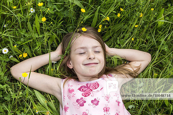 Porträt eines lächelnden Mädchens mit geschlossenen Augen auf einer Blumenwiese liegend