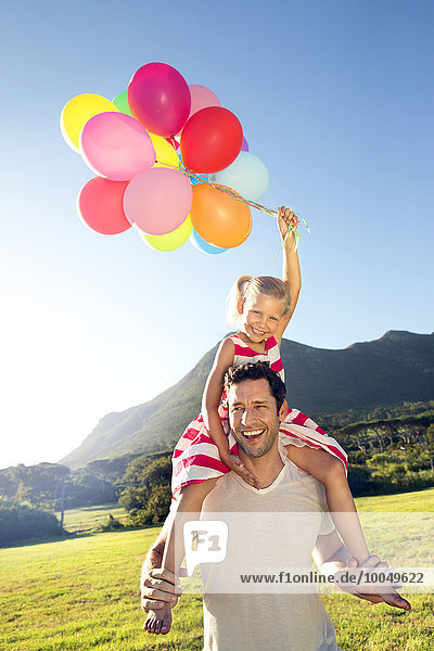 Glücklicher Vater trägt Tochter mit Ballons auf den Schultern