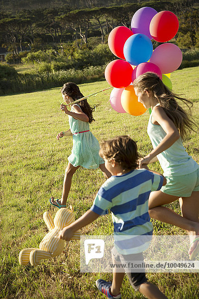 Glückliche Kinder laufen mit Luftballons auf der Wiese