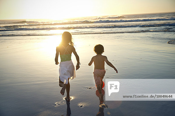 Junge und Mädchen laufen bei Sonnenuntergang am Strand.