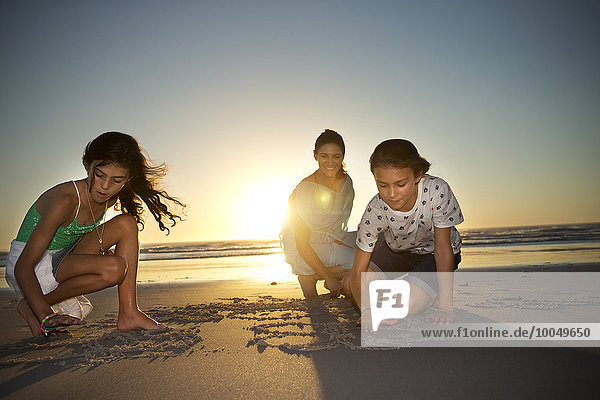 Mutter mit Töchtern am Strand bei Sonnenuntergang Zeichnung in Sand