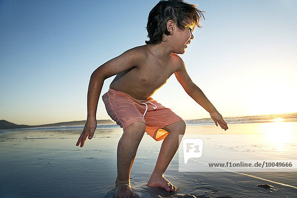 Junge spielt am Strand bei Sonnenuntergang