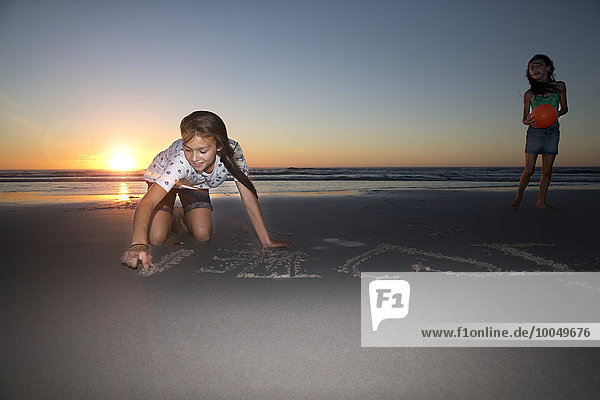 Mädchen am Strand bei Sonnenuntergang Zeichnung in Sand