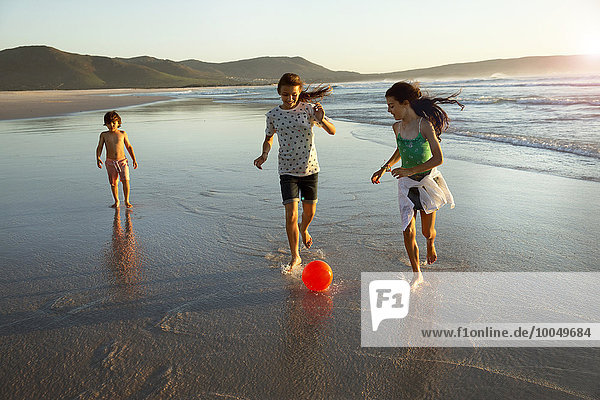 Drei Kinder spielen mit dem Ball am Meer