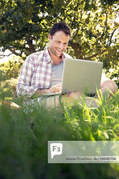 Lächelnder Mann mit Laptop auf der Wiese sitzend