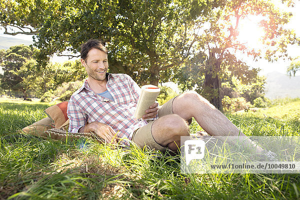 Lächelnder Mann auf der Wiese liegend Lesebuch